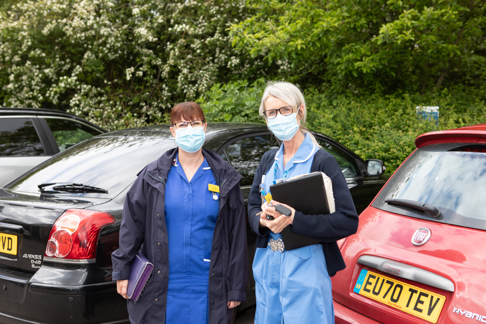 2 community nurses stood next to their vehicles