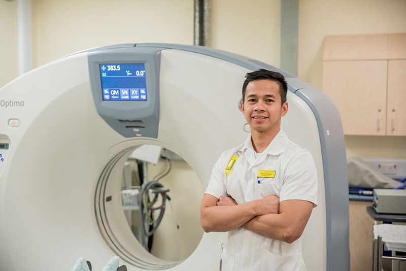 A man stands with arms folded in front of a ct scanner
