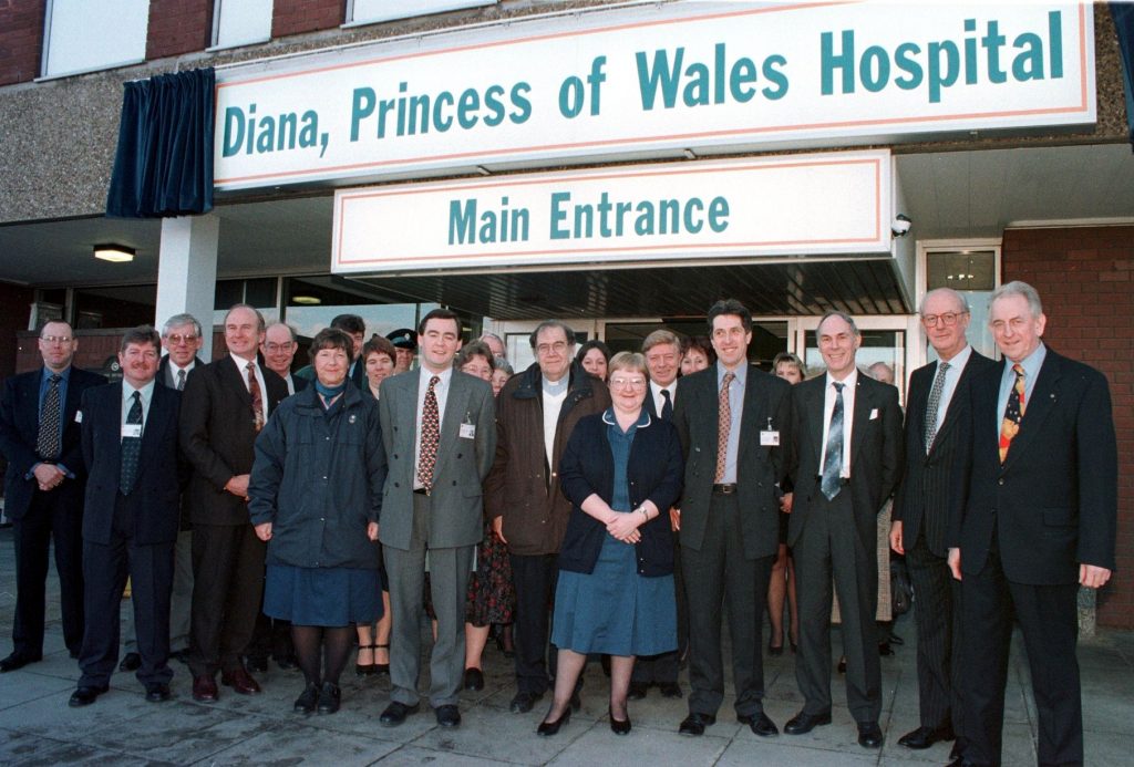 A large group of people stand beneath the newly unveiled sign showing the hospital's new name: Diana, Princess of Wales Hospital