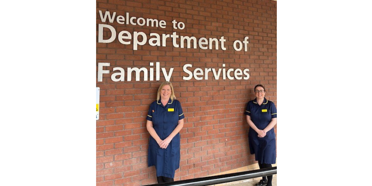 Two nurses in a blue uniform are standing against a wall which says Department of Family Services