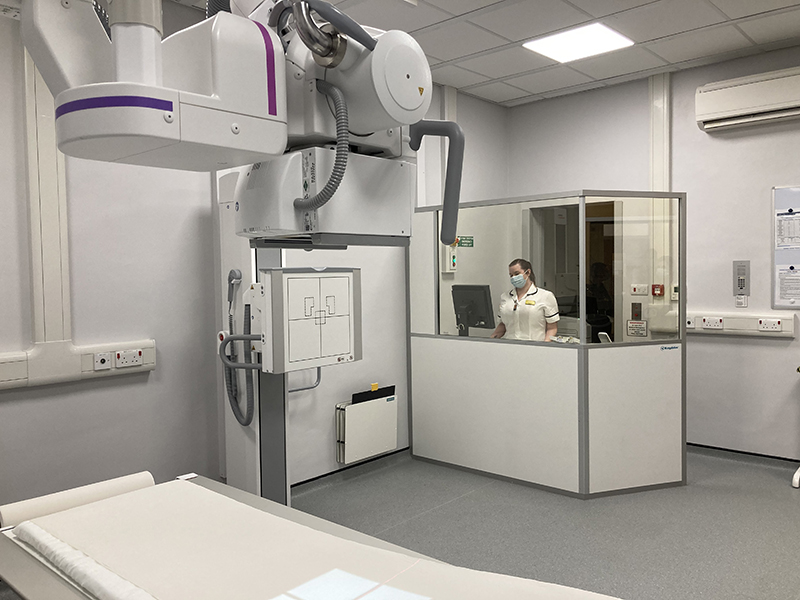 A radiographer stands behind the glass in an Xray room