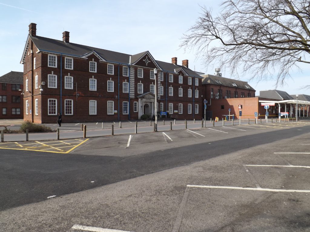 The exterior of the former Administration Block. The main entrance, has a memorial archway, there are a number of white-framed windows and four chimneys.