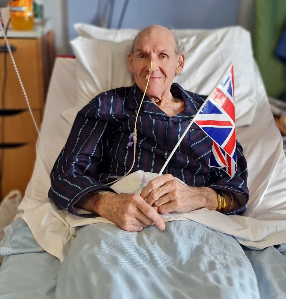 Patient Barrie in a hospital bed waving British flag