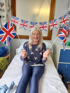 Patient Elaine in hospital bed waving two British flags