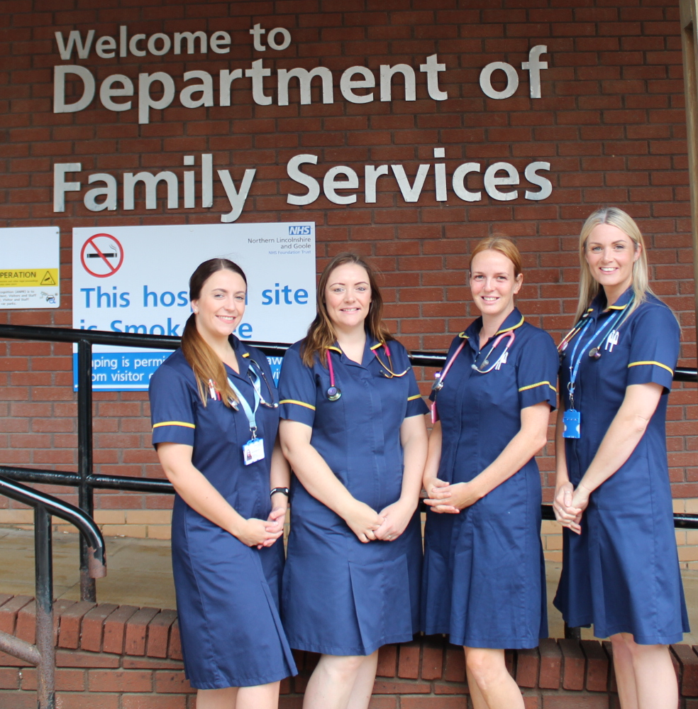 Four nurses in uniform stood outside a sign saying 'Welcome to department of Family Services'.