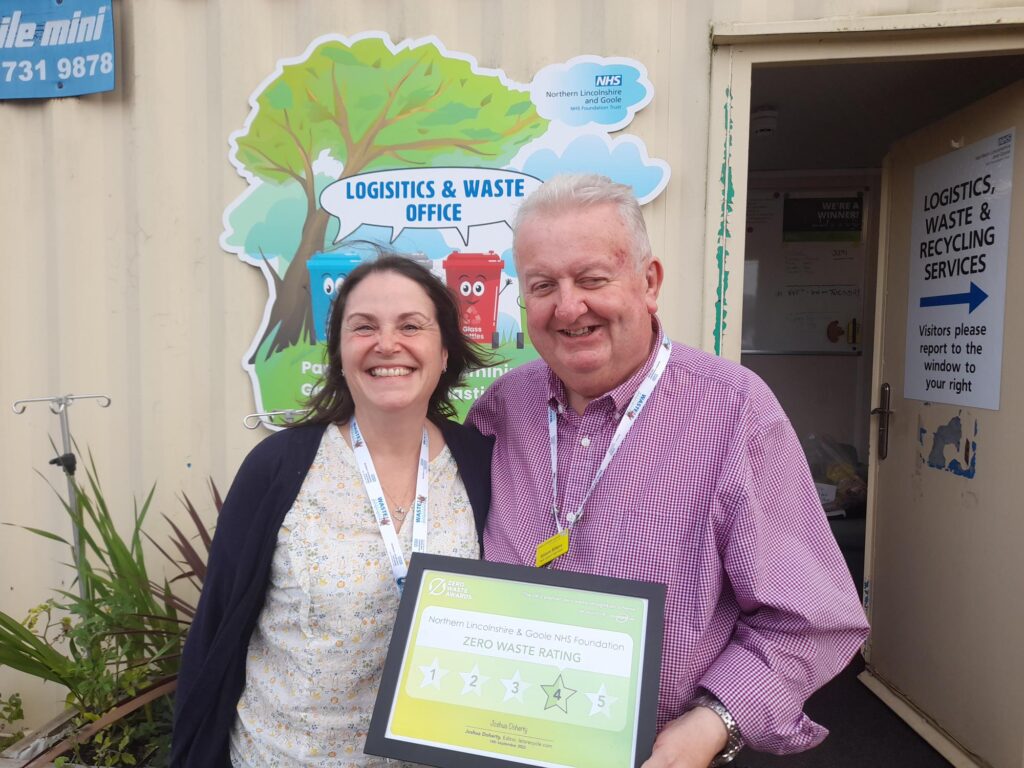 A woman and a man stood smiling and holding a framed four-star Zero Waste Award.