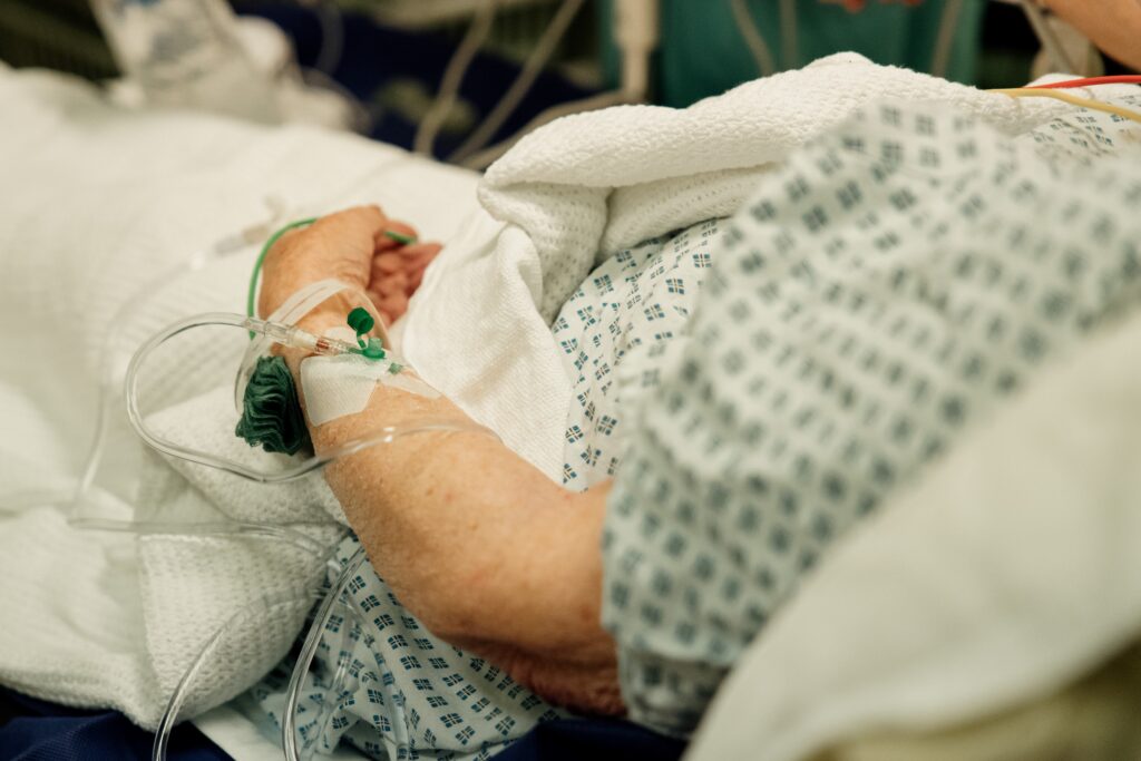 a patient dressed in a hospital gown with wires in their arm lays in a bed
