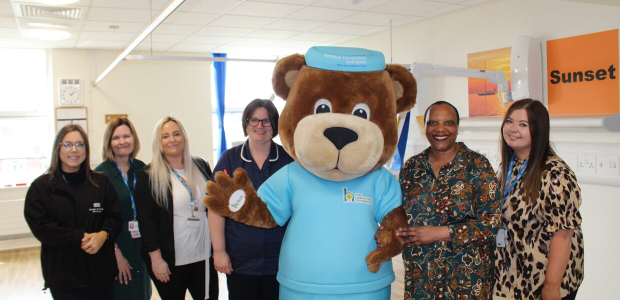 A woman stood next to a giant bear with charity and NHS staff
