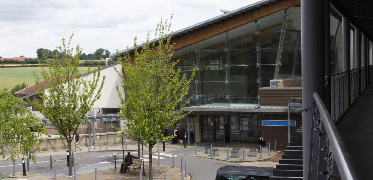 Exterior shot of Queen's Centre with three trees in the foreground and a TASL ambulance parked in a bay close to the entrance