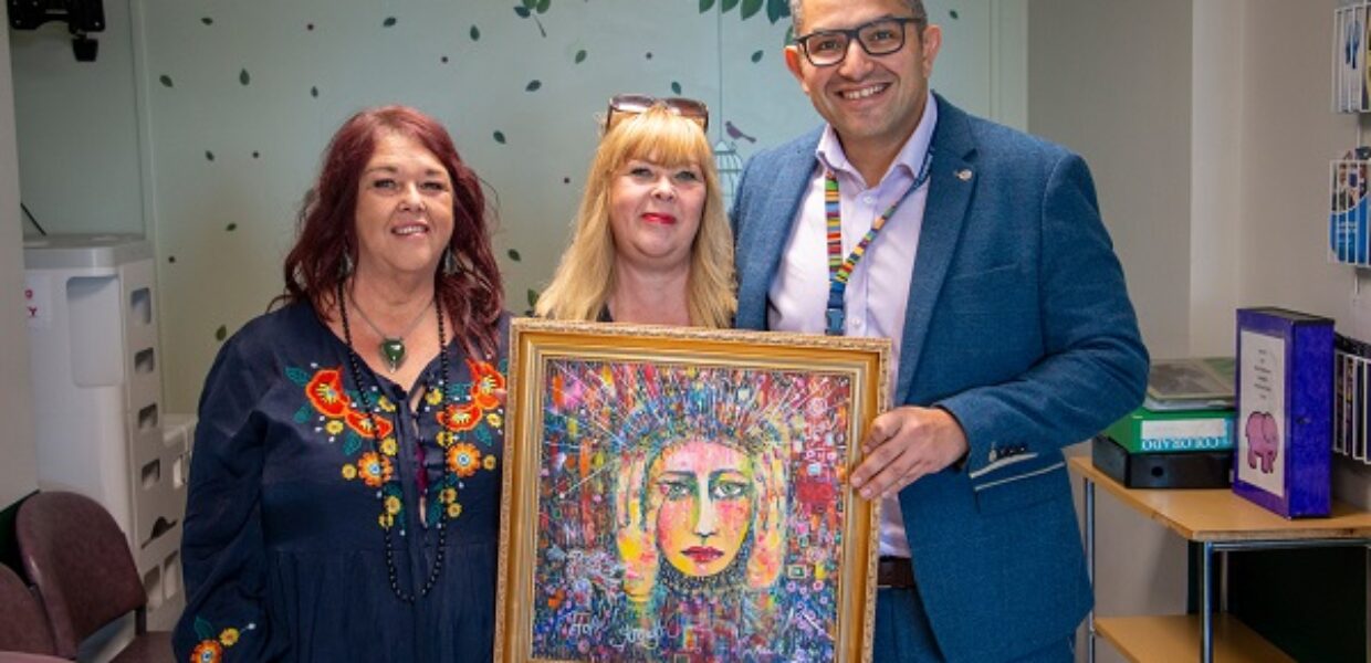 Nicola Crofts stands in the centre, holding the painting, with Mr Adam Razak on her left and her sister Michelle Pearson on her right