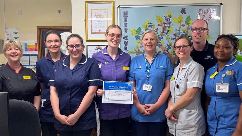 A line up of healthcare professionals with a woman standing in the middle holding a certificate