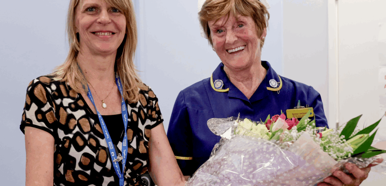 Two women smiling and holding a bunch of flowers. One is wearing a nurse's uniform
