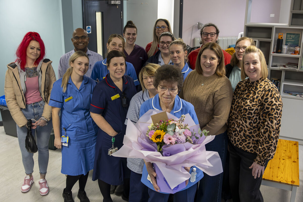 A group of people, some wearing clinical uniforms, pictured with a nurse holding flowers
