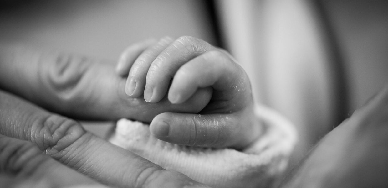 BLACK AND WHITE IMAGE OF A BABY'S HAND GRIPPING AN ADULT'S FINGER