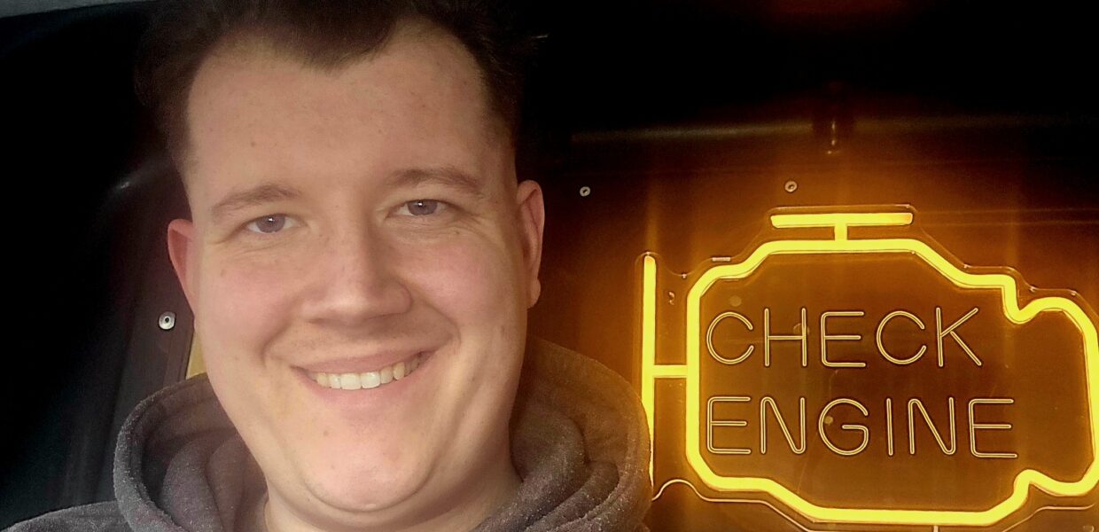 A man stood smiling in front of a neon sign