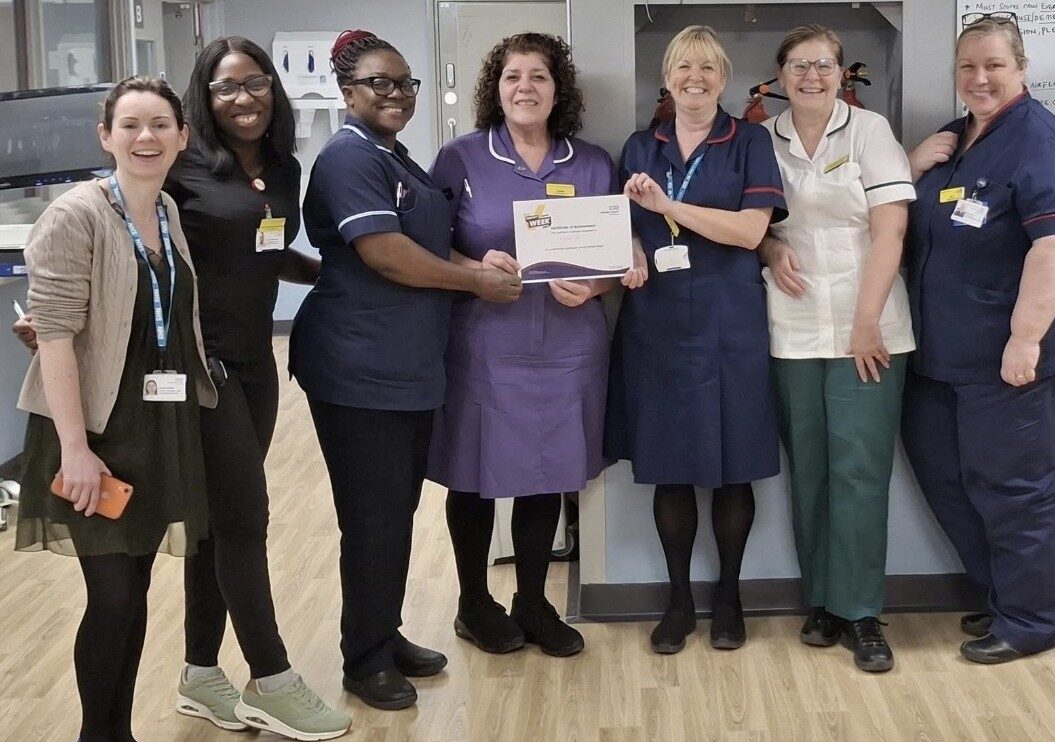 A group of NHS staff on a hospital ward. A certificate is being presented