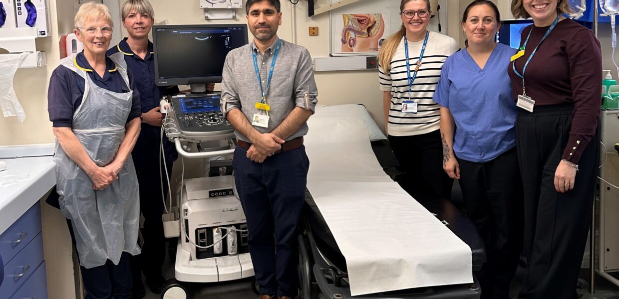A group of hospital staff in a clinic room, stood near a bed and a machine