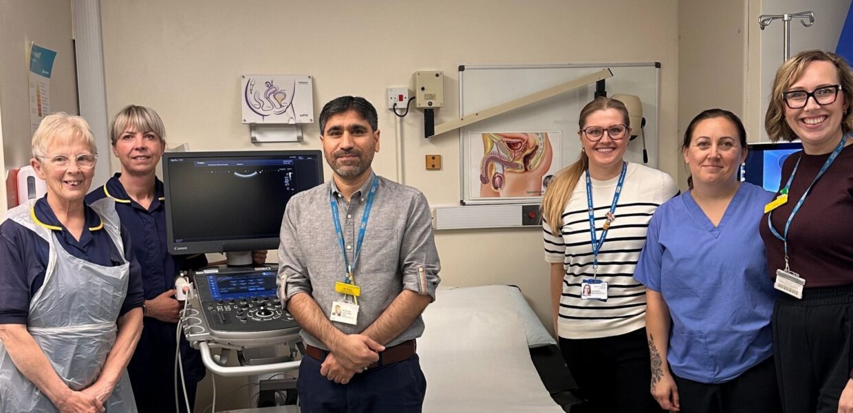 A group of hospital staff in a clinic room, stood near a bed and a machine