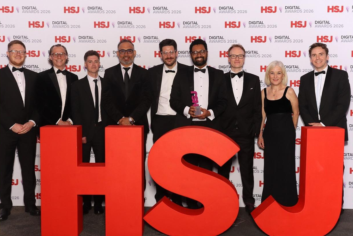 NHS colleagues pictured at an awards ceremony. One is holding a trophy and they're stood in front of a HSJ banner