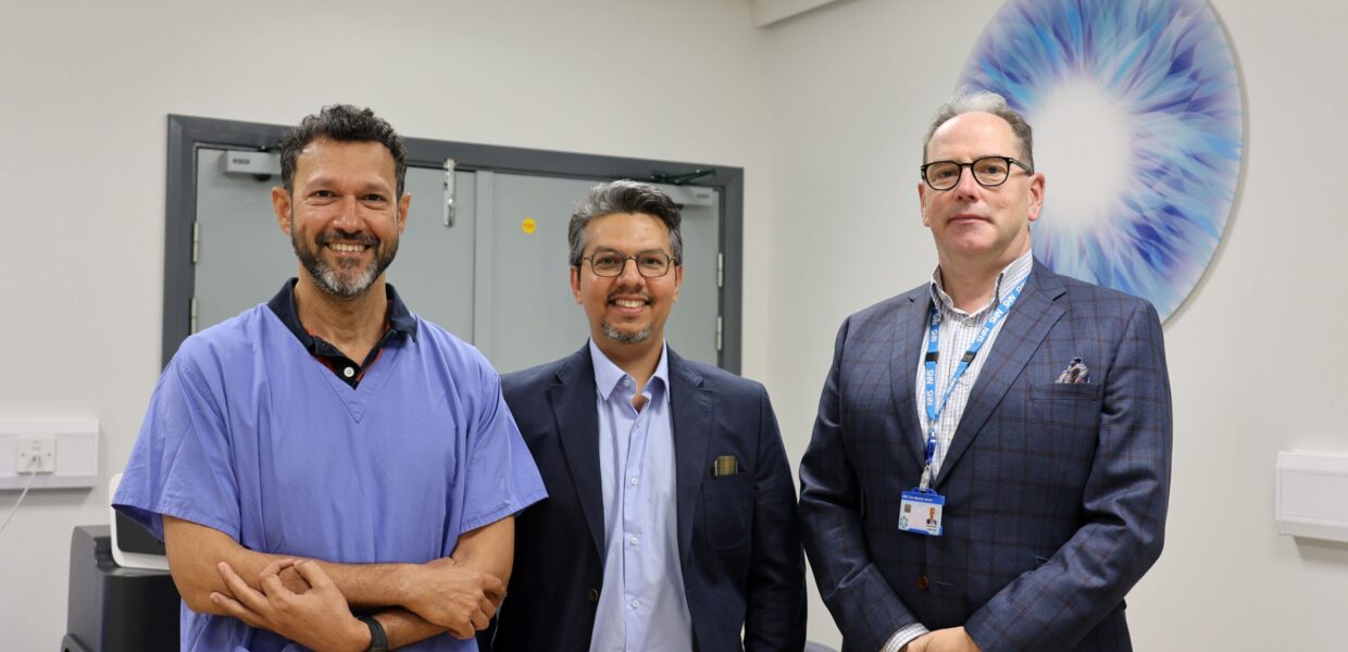 Three men in a clinic room. One is wearing scrubs, the other two are in formal wear