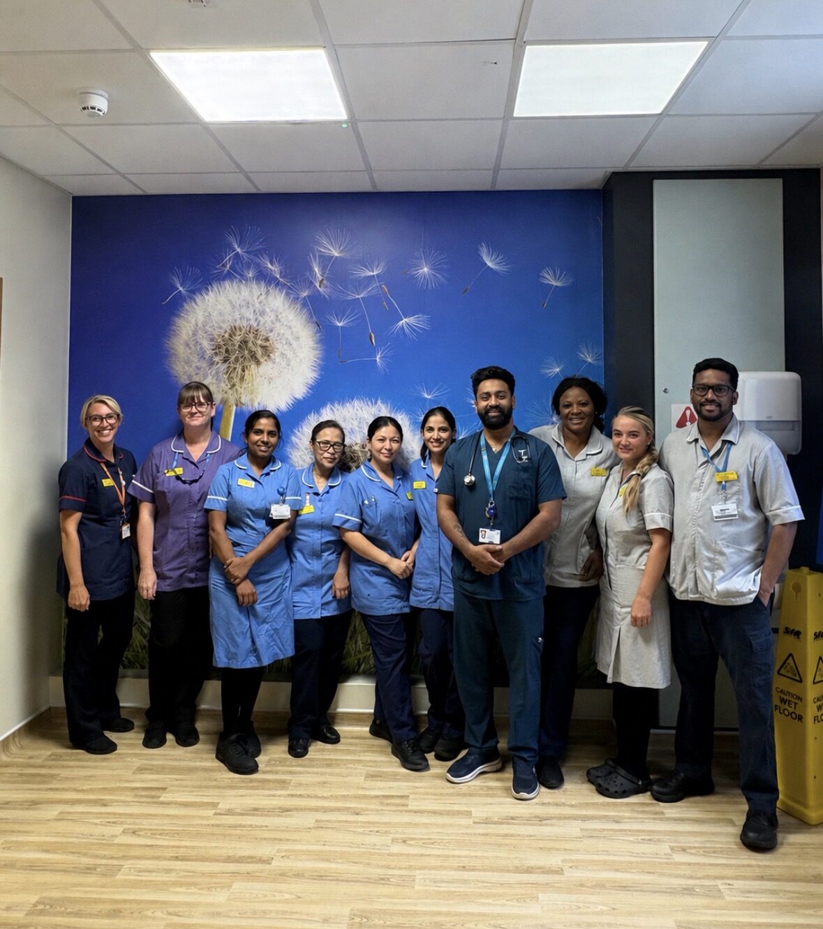 A group of hospital staff on a ward, stood in front of a mural