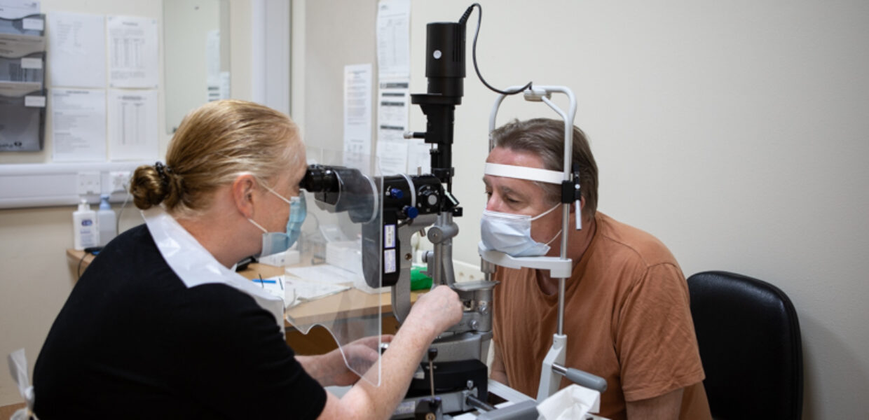 A woman is sitting at a desk with a special piece of equipment which is looking into a patients eyes.