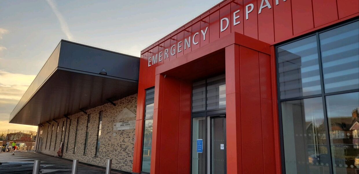the Scunthorpe Emergency Department at sunset. The doorway of the building is glass, surrounded by red cladding.