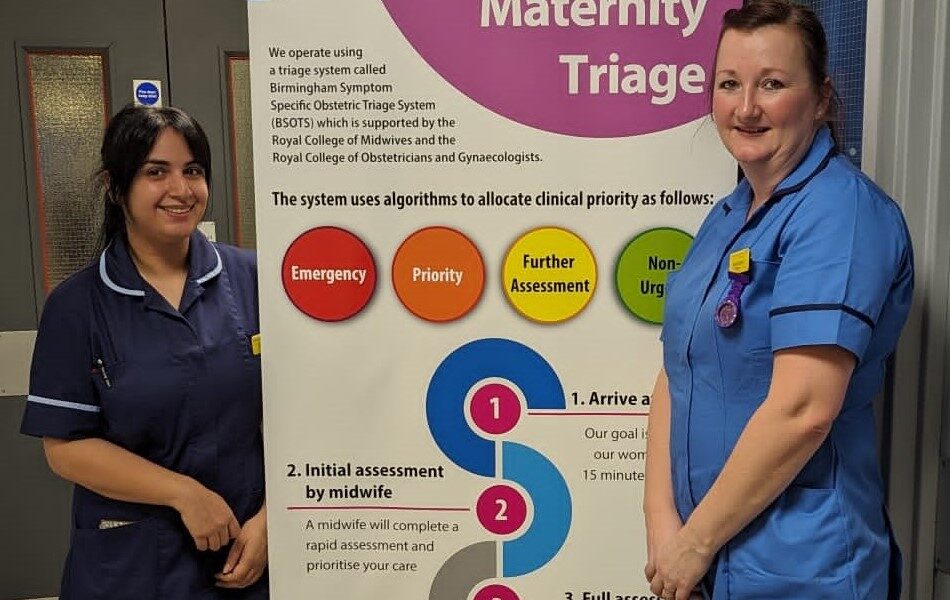 Two midwives stood in front of a pull-up banner