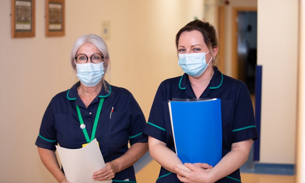 Two nurses standing in a corridor, holding files