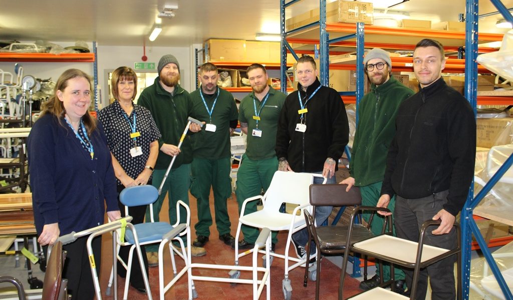 a group of staff stood with variois medical aids including walking sticks and shower chairs