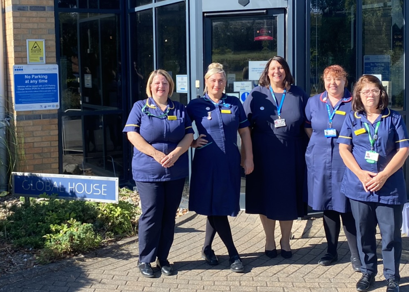 Five members of senior nursing staff stand together outside in their dark blue nursing tunics